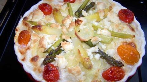 Ein köstlicher Spargelauflauf mit frischem Spargel, Tomaten und Käse, leicht gebräunt im rotem Auflaufform.