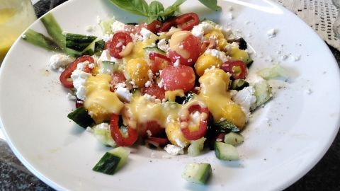 Ein bunter Melonensalat mit Mango und Feta wird auf einem weißen Teller angerichtet und mit frischen Kräutern garniert.