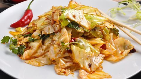 Eine großzügige Portion Chinakohl-Gemüse-Pfanne liegt auf einem weißen Teller, bedeckt mit frischem Koriander und einer roten Chilischote.