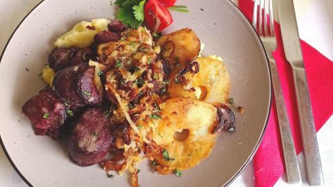 Ein Teller mit Himmel und Erde, bestehend aus Blutwurst, Kartoffelpüree und gebratener Zwiebel, garniert mit Tomaten.
