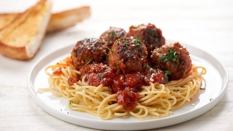 Saftige Hackbällchen liegen auf einer Portion Spaghetti, die in Tomatensoße getaucht sind, mit geröstetem Brot daneben.