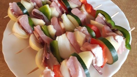 Bunte Schaschlik-Spieße mit Fleisch und Gemüse liegen schön auf einem weißen Teller auf einem Holztisch.