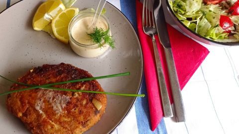 Fischfrikadellen liegen auf einem Teller, daneben stehen Zitronenscheiben und ein Dip; frisch zubereitete Beilagen ergänzen das Gericht.