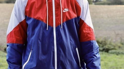 Ein junger Mann trägt eine alte Jacke in Rot und Blau, während er in einem offenen Feld steht, bereit für ein Upcycling-Projekt.