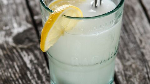 Ein Glas mit einem erfrischenden Killerdrink, gefüllt mit einer hellen Flüssigkeit, einem Strohhalm und einer Zitronenscheibe, steht auf Holz.