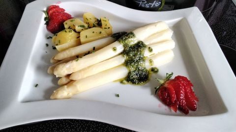 Weißer Spargel liegt auf einem Teller, garniert mit Bärlauch-Pesto, dazu Kartoffeln und Erdbeeren. Frisch und ansprechend.