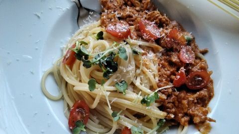 Spaghetti liegen neben Hähnchen-Bolognese, garniert mit Tomaten und Kräutern auf einem weißen Teller.