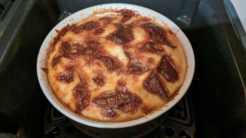 Ein runder, goldbrauner Schoko-Bananen-Kuchen backt in einer Heißluftfritteuse und verbreitet einen köstlichen Duft.