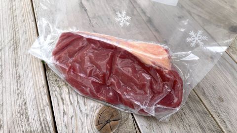 Ein vakuumierter Beutel mit Fleisch liegt auf einer Holzoberfläche, während Wasser um den Beutel herum ist.