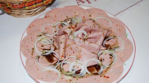 Auf einem Teller liegt eine sorgfältig angerichtete Extrawurst mit Zwiebeln, verfeinert mit Essig und Öl.