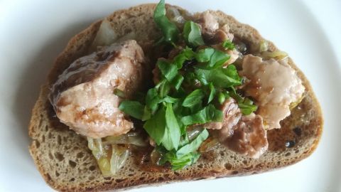 Auf einer Scheibe Brot liegt Dorschleber, garniert mit karamellisierten Zwiebeln und frischem grünen Blattwerk.