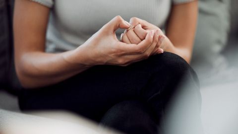 Eine Person sitzt entspannt auf einem Sofa und drückt ihre Hände zusammen, um Nervosität zu bekämpfen.