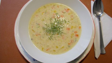 Eine Schüssel Rote Linsensuppe steht auf einem Tisch, garniert mit Kräutern, umgeben von Besteck und einer Serviette.