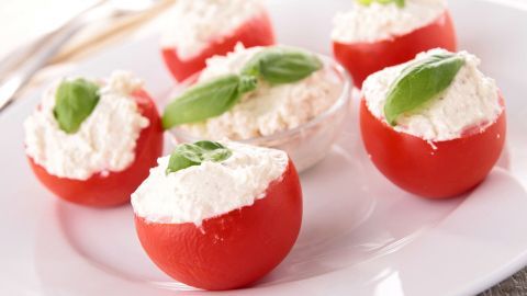 Gefüllte Tomaten mit Frischkäse stehen auf einem weißen Teller, dekoriert mit frischem Basilikum.