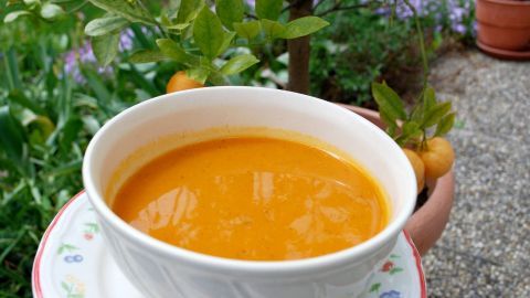 Eine cremige Kürbissuppe in einer weißen Schüssel wird vor einem Garten mit Calamondin-Orangen und grünen Pflanzen präsentiert.