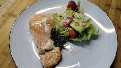 Auf einem Teller liegt ein gebratener Lachs, serviert mit buntem Kopfsalat und einer Kräutermayonnaise.