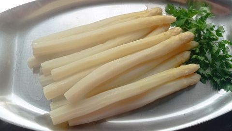 Auf einem silbernen Teller liegen frische, weiße Spargelstangen, neben denen frische Petersilie dekorativ platziert ist.