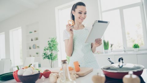 Eine Frau in einem hellen Küchenraum hält ein Tablet und lächelt, während sie eine Zutatenliste für E-Books überprüft.