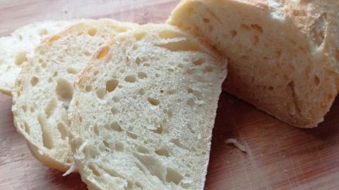 Ein frisch gebackenes Brot liegt auf einem Holzbrett, mit geschnittenen Scheiben daneben, die eine luftige Textur zeigen.