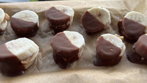 Runde Bananenstücke mit Schokolade überzogen liegen auf braunem Papier, ideal für einen süßen Snack.