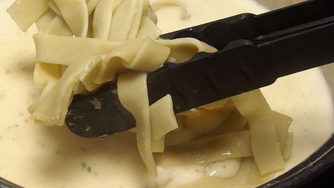 Nudeln werden mit einer Zange aus einer cremigen Sauce in einem Topf entnommen, um sie lecker aufzuwärmen.
