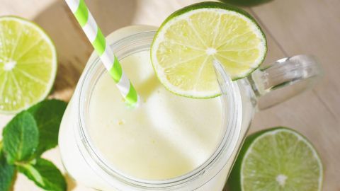Ein Glas brasilianische Limonade steht auf einem hellen Tisch, umgeben von Limetten und Minzblättern.