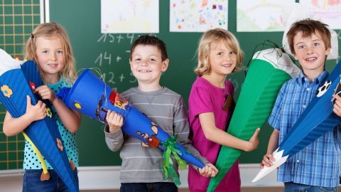 Vier Kinder halten stolz ihre bunten Schultüten in einem Klassenzimmer vor einer Tafel. Freude zur Einschulung!
