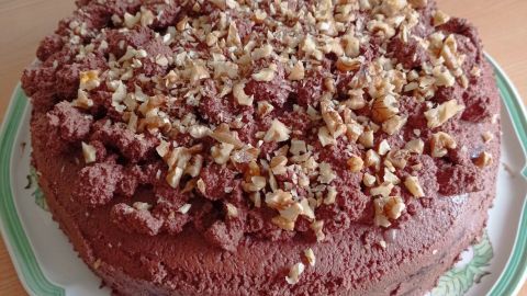 Eine Walnuss-Schoko-Torte steht auf einem Tisch, dekoriert mit gehackten Walnüssen und einer schokoladigen Glasur.