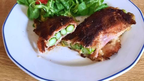 Panierter Spargel mit Käse und Schinken fällt auf einem Teller, umgeben von frischem Salat und Beeren.