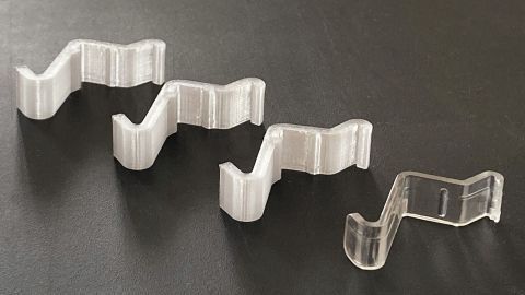 Transparente Befestigungsclips für Wandlampen liegen auf einem dunklen Tisch und sind bereit zum Nachbauen für DIY-Projekte.