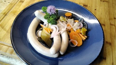 Auf einem blauen Teller liegen fränkische Bratwürste, umgeben von buntem Gemüse und frischen Kräutern.