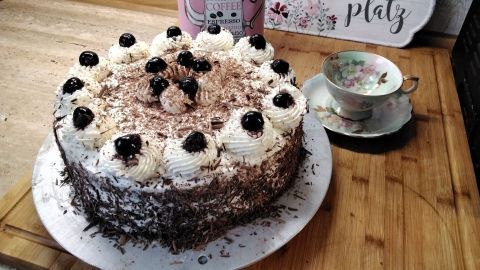 Eine Schwarzwälder Kirschtorte steht dekorativ auf einem Tisch, umgeben von einer Tasse und einem nostalgischen Kaffeebehälter.