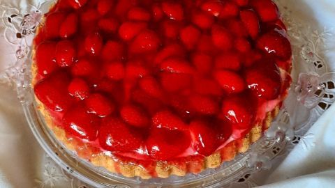 Ein Erdbeerkuchen mit glänzender Erdbeerschicht ruht auf einer schönen, weißen Tischdecke.
