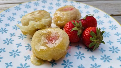 Gebackene Erdbeeren liegen auf einem blauen Teller, umgeben von frischen Erdbeeren, alle mit glänzendem Honig.