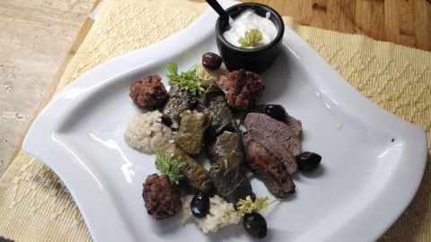 Gefüllte Weinblätter liegen auf einem weißen Teller, umgeben von Hackfleischbällchen und Reis, serviert mit Joghurt.