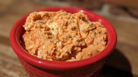 Ein rot-orangefarbener Dip ist in einer roten Schüssel angerichtet, bereit zum Genießen auf einer Holzoberfläche.