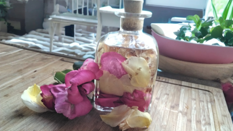 Eine Glasflasche mit Rosenblättern steht auf einem Holztisch, umgeben von einer hellen, gemütlichen Küche.