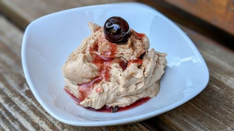 Eine cremige Schoko-Mascarpone-Creme wird in einer weißen Schale serviert, garniert mit einer Kirsche und Fruchtsauce.
