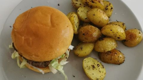 Ein Hamburger liegt auf einem Teller und wird von mediterranen Ofenkartoffeln begleitet, alles appetitlich angerichtet.