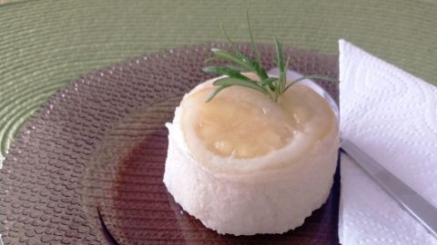 Zitronen-Grießpudding liegt auf einem glänzenden Teller, garniert mit einer Zitronenscheibe und frischem Kräuterzweig.