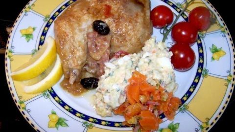 Zarte Hähnchenschenkel liegen auf einem bunten Teller, begleitet von Kartoffelsalat und frischen Tomaten.