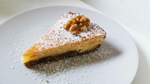 Ein Stück Zitronen-Walnuss-Kuchen liegt auf einem weißen Teller, mit Puderzucker bestreut und einer Walnuss obendrauf.