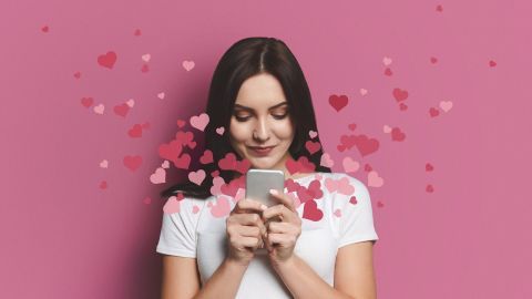 Eine Frau hält ein Smartphone und lächelt, umgeben von rosefarbenen Herzen, was die Freude am Online-Dating symbolisiert.