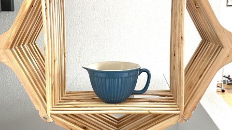 Ein hängendes Regal aus Kleiderbügeln zeigt eine blaue Schüssel, die elegant in einem modernen Raum platziert ist.