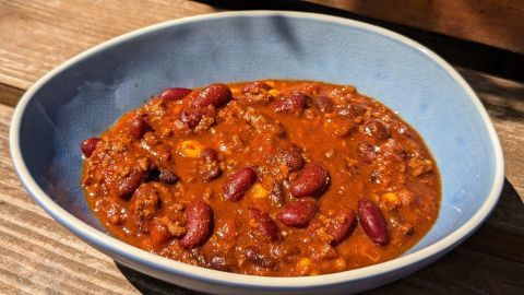 Ein blauer Teller mit Chili con Carne, reichhaltig und würzig, steht auf einer Holzoberfläche im Freien.