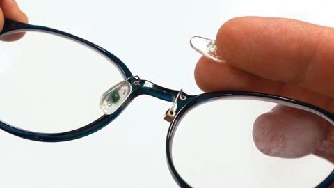 Eine Hand hält eine Brille, während das Nasenpad gewechselt wird, auf einem neutralen Hintergrund sichtbar.