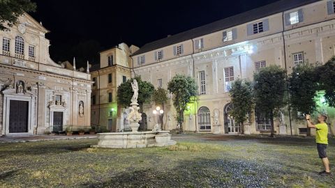 Eine Statue steht an einem Brunnen, während ein Mann in gelbem Shirt Fotos in einem beleuchteten Innenhof nachts macht.