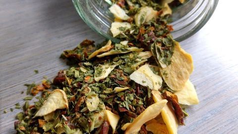 Ein Glas mit getrockneten Kräutern kippt, während der Inhalt auf eine Holzoberfläche streut, wunderbar für ein Kräuter-Pesto.