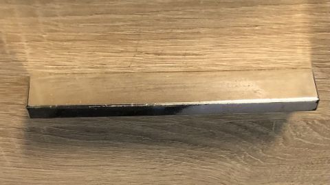 Ein Möbelgriff aus Metall lehnt an einem hellen Holzregal, während ein anderer darunter mit Deko-Klebeband gestaltet ist.