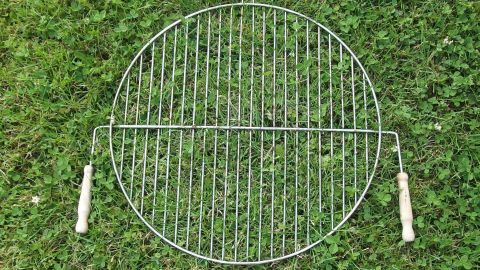 Ein Grillrost liegt auf dem gr&uuml;nen Gras. Er ist oval, mit zwei Holzgriffen und bereit zum Reinigen.